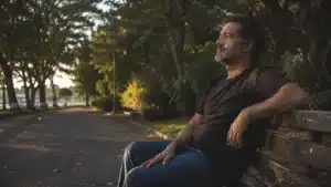 Homem sentado em um banco de parque, em clima contemplativo, durante o fim da tarde.